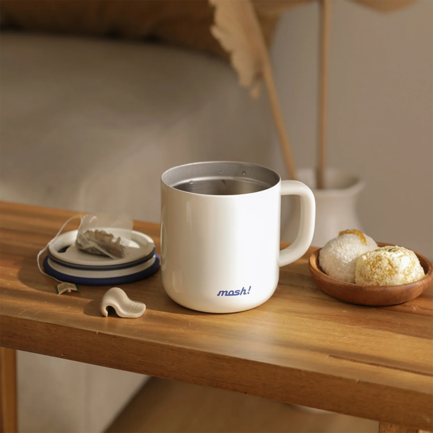 White mug with 'mosh!' branding on a wooden table with tea leaves and a teacup.